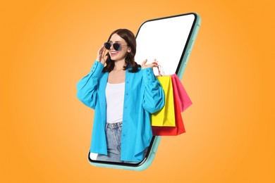 Image of Online shopping. Happy woman with paper bags looking out from smartphone on orange background