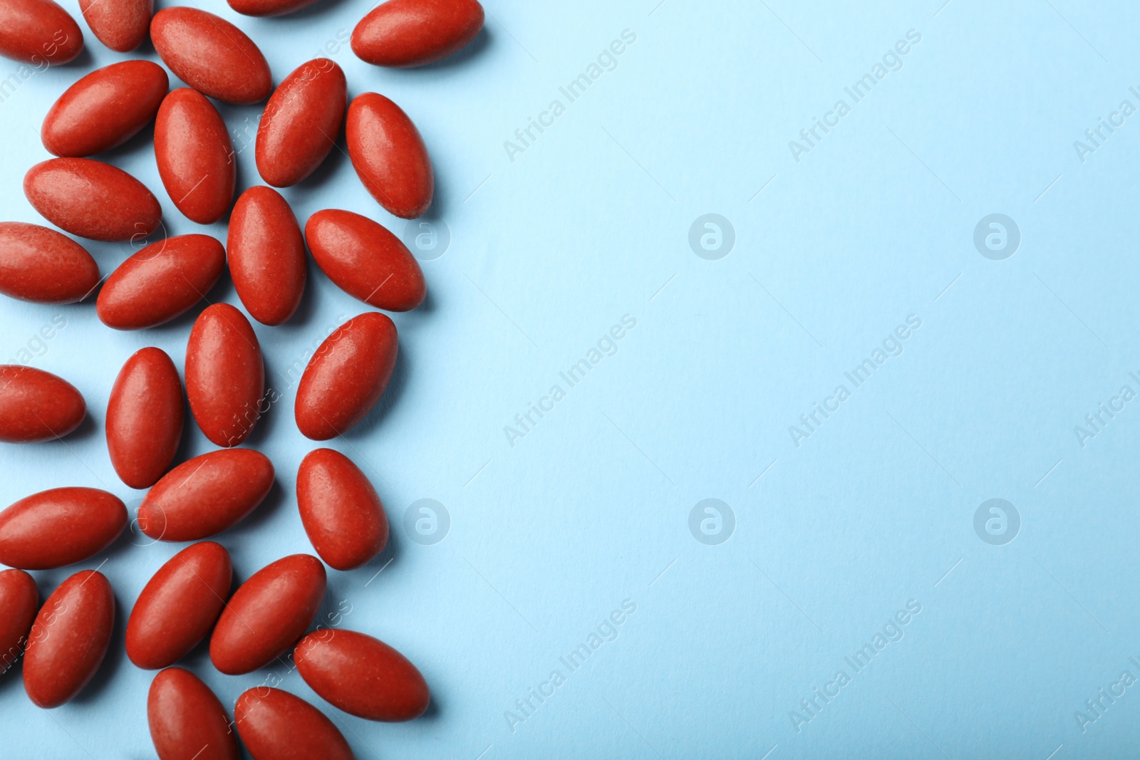 Photo of Red pills on light blue background, flat lay with space for text. Anemia treatment