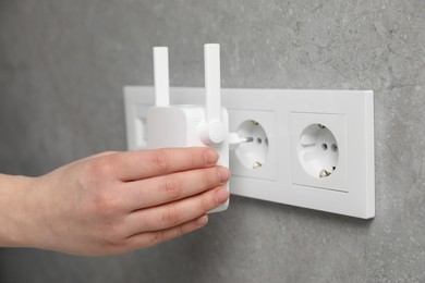 Photo of Woman turning on wireless Wi-Fi repeater indoors, closeup