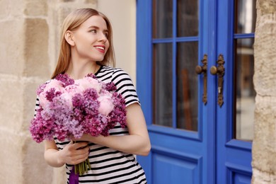 Photo of Beautiful woman with bouquet of spring flowers near building outdoors, space for text