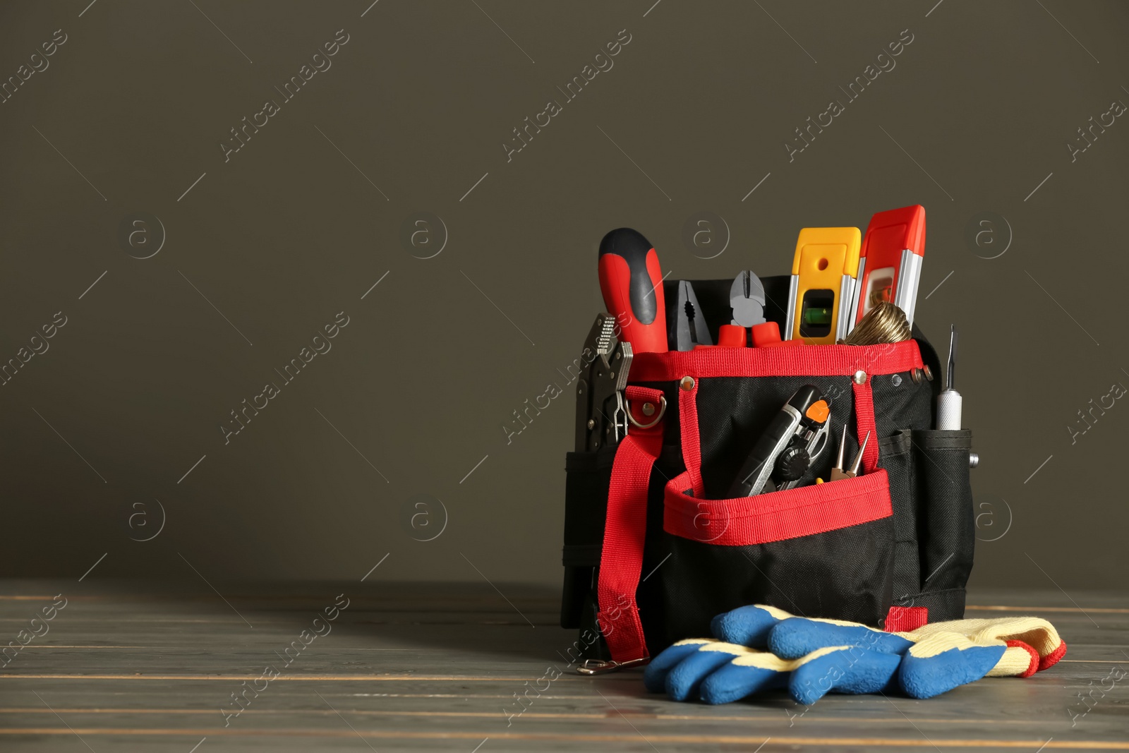 Photo of Bag with different tools for repair and protective gloves on wooden table, space for text