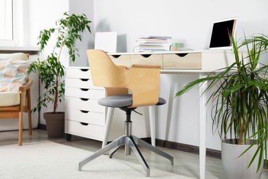 Photo of Beautiful workplace with laptop on white wooden table, chair and houseplants in room