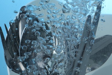 Photo of Washing silver cutlery in water on light blue background, closeup