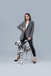 Beautiful young woman with her adorable Dalmatian dog on light grey background. Lovely pet