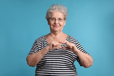 Elderly woman making heart with her hands on light blue background