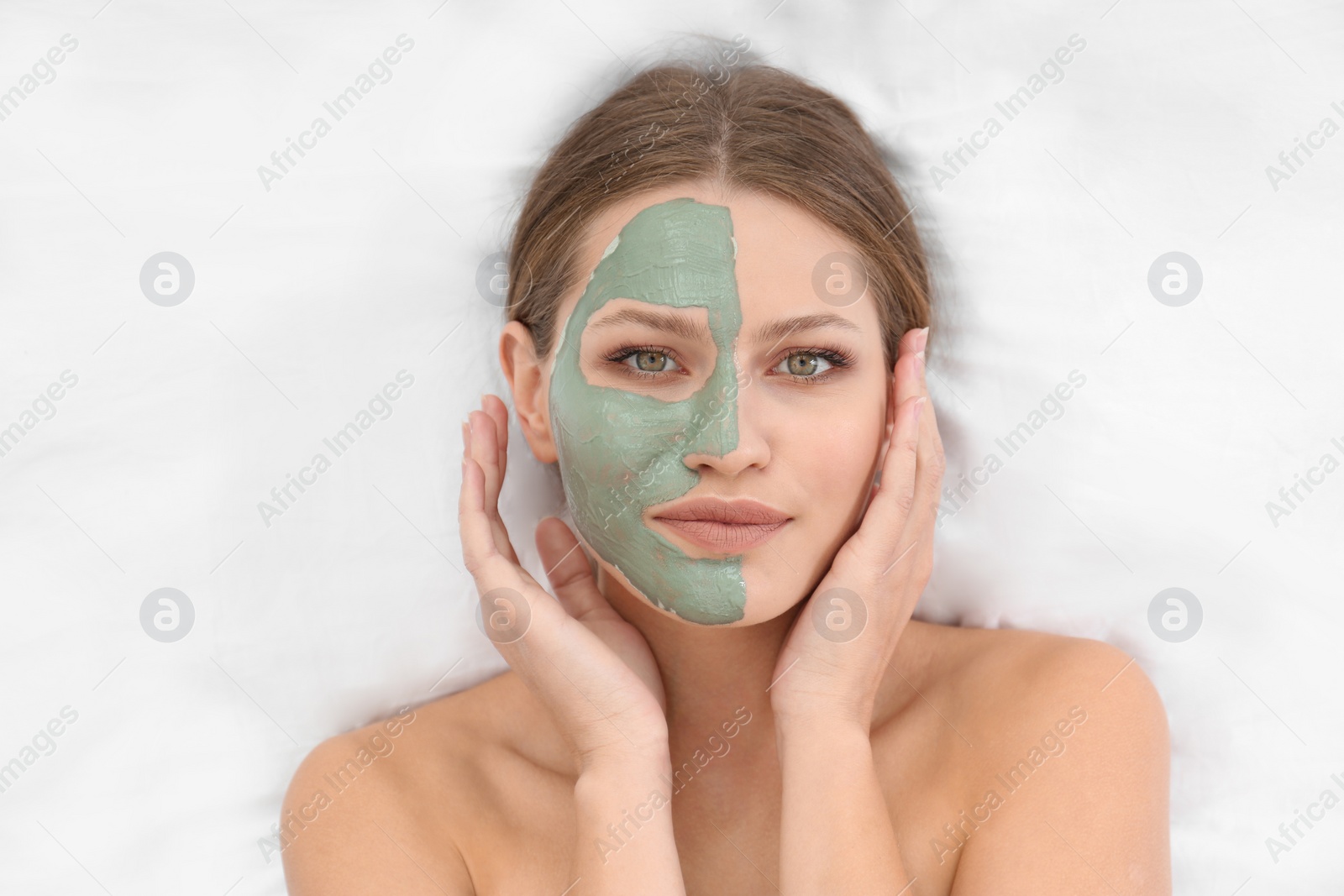 Photo of Beautiful woman with clay facial mask on white fabric, above view