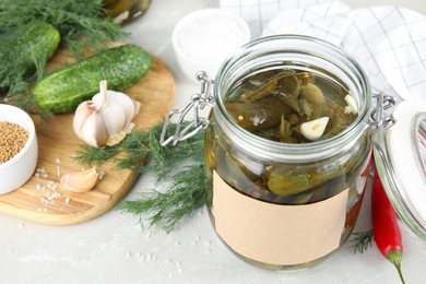 Photo of Jar of pickled cucumbers with blank sticker on grey table, space for text