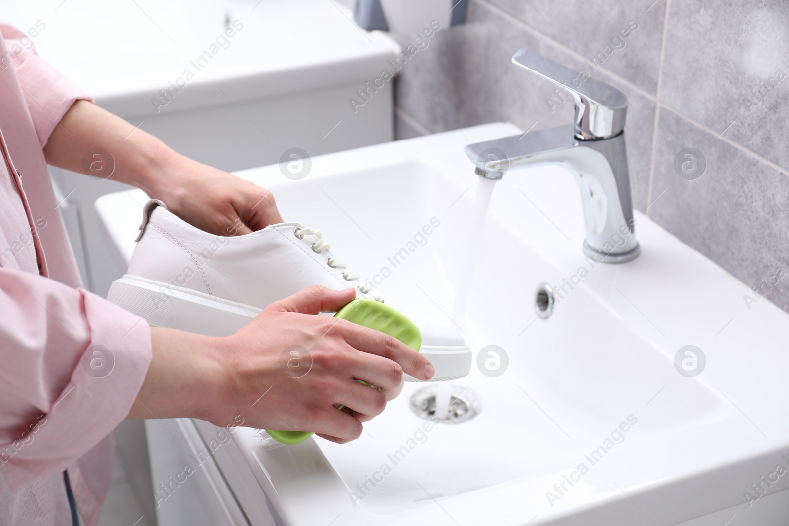 Photo of Woman washing stylish sneakers with brush in sink, closeup