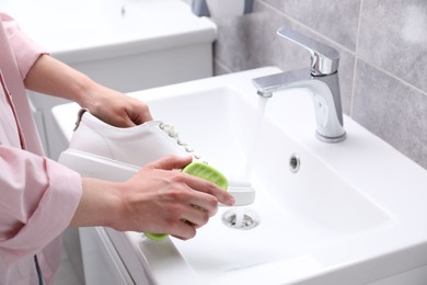 Woman washing stylish sneakers with brush in sink, closeup