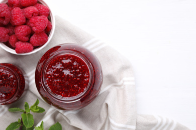 Delicious jam and fresh raspberries on white wooden table, flat lay. Space for text