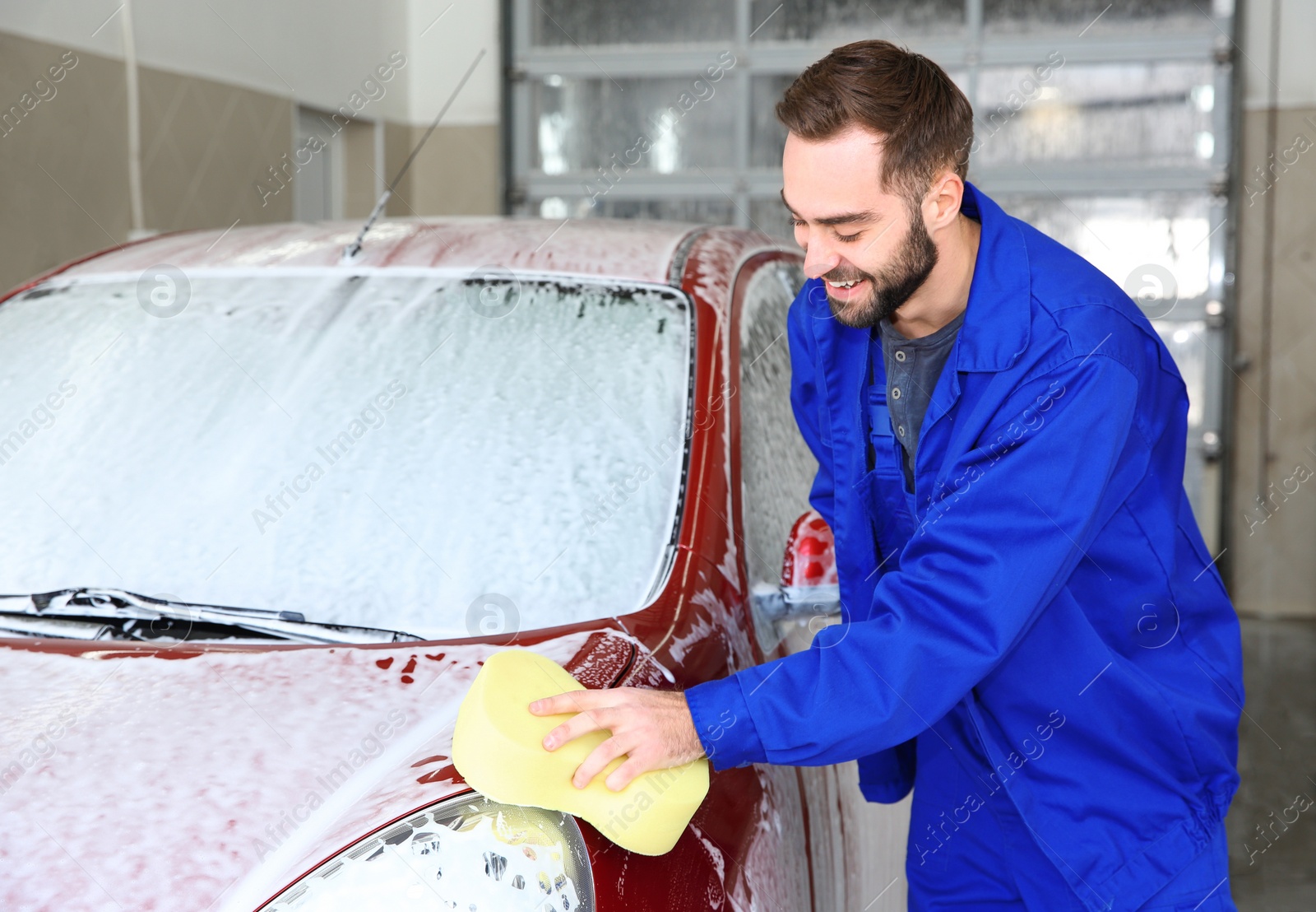 Photo of Worker cleaning automobile with sponge at professional car wash