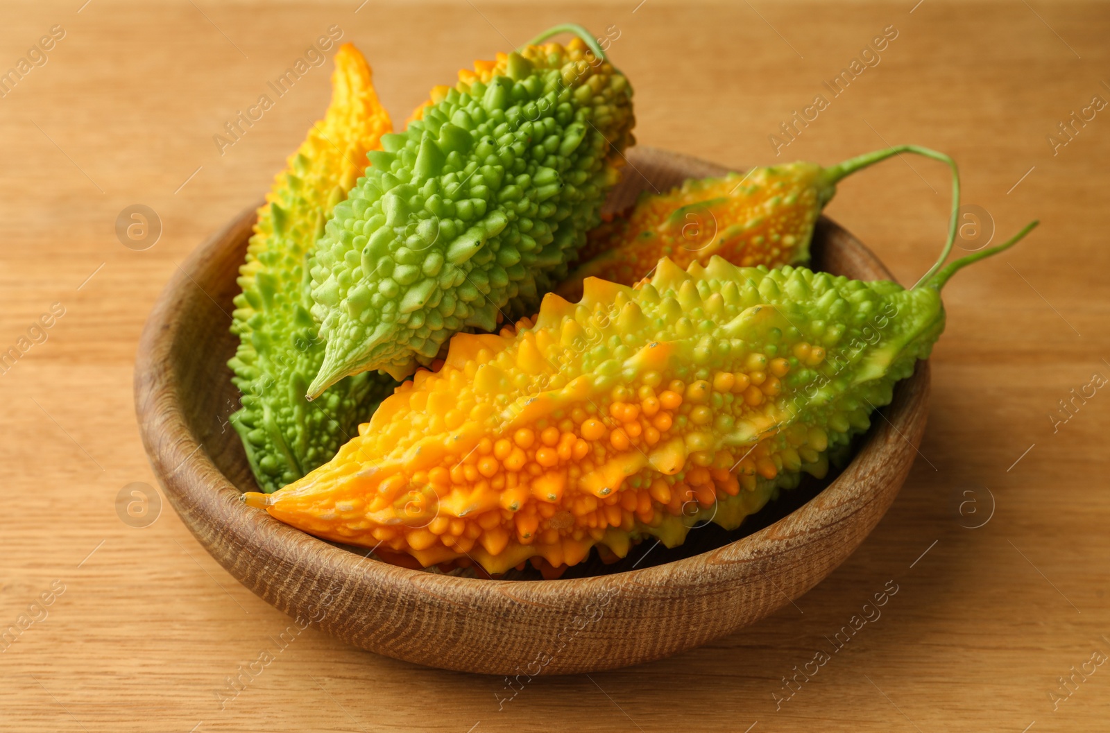 Photo of Bowl with fresh bitter melons on wooden table, closeup