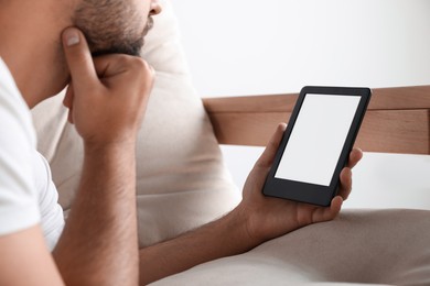 Photo of Man using e-book reader on sofa indoors, closeup