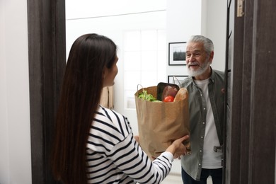 Photo of Courier giving paper bag with food products to senior man indoors