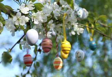 Photo of Beautifully painted Easter eggs hanging on blooming tree outdoors, space for text