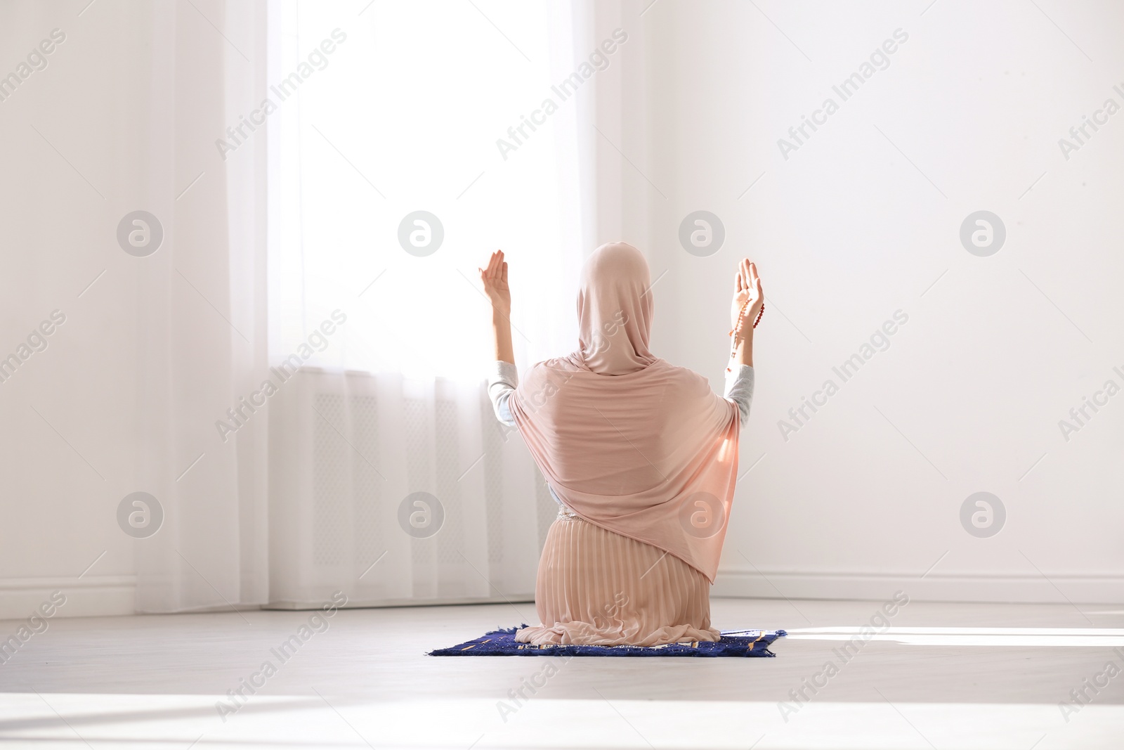 Photo of Muslim woman in hijab praying on mat indoors