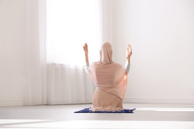 Photo of Muslim woman in hijab praying on mat indoors