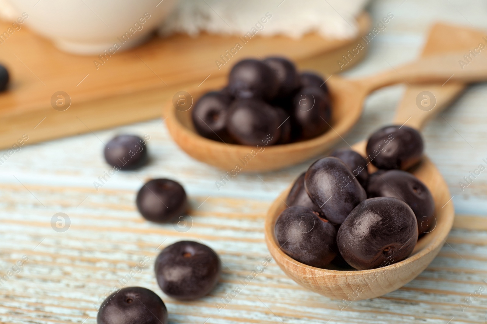 Photo of Spoons of fresh acai berries on light wooden table, closeup. Space for text