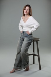 Photo of Beautiful young woman near stool against grey background