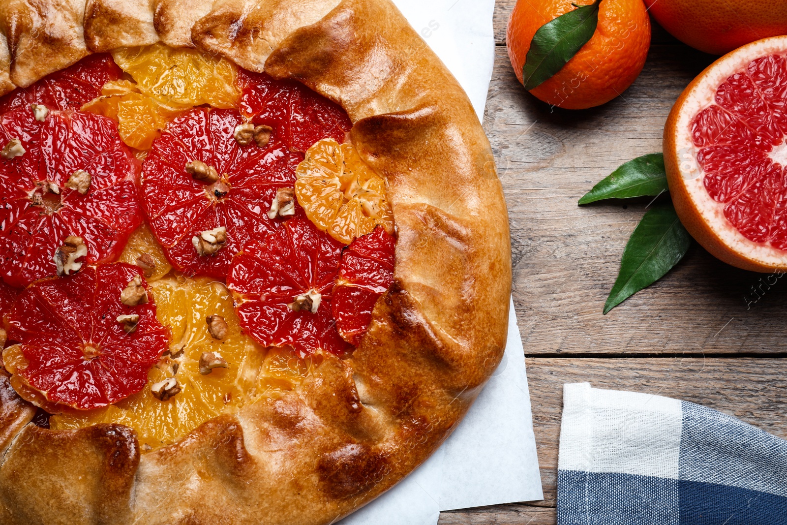 Photo of Delicious galette with citrus fruits and walnuts on wooden table, flat lay