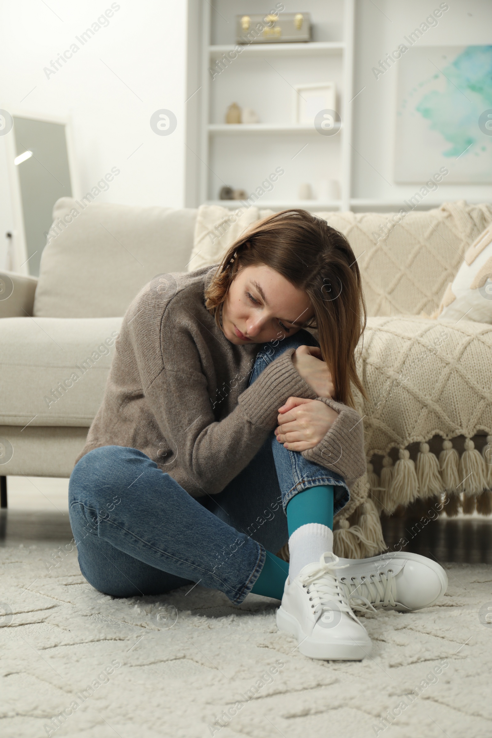 Photo of Sad young woman sitting on floor at home