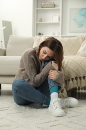 Sad young woman sitting on floor at home