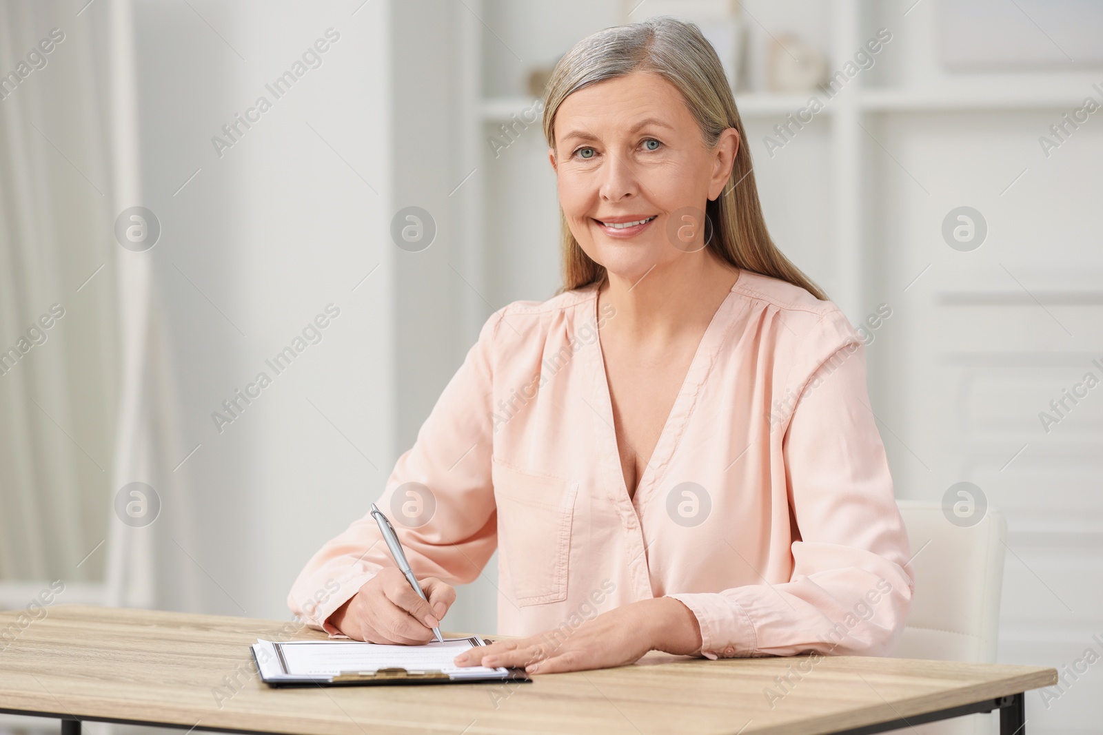 Photo of Smiling senior woman signing Last Will and Testament at wooden table indoors