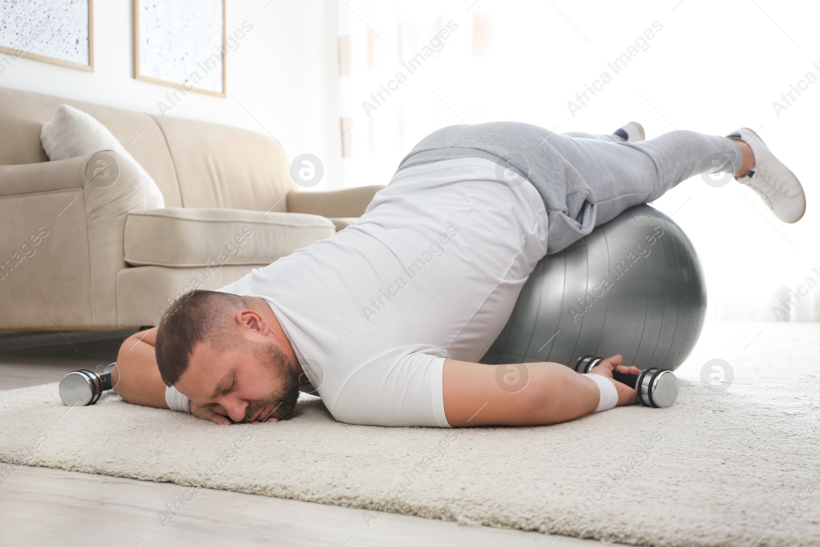 Photo of Lazy overweight man with sport equipment sleeping on floor at home