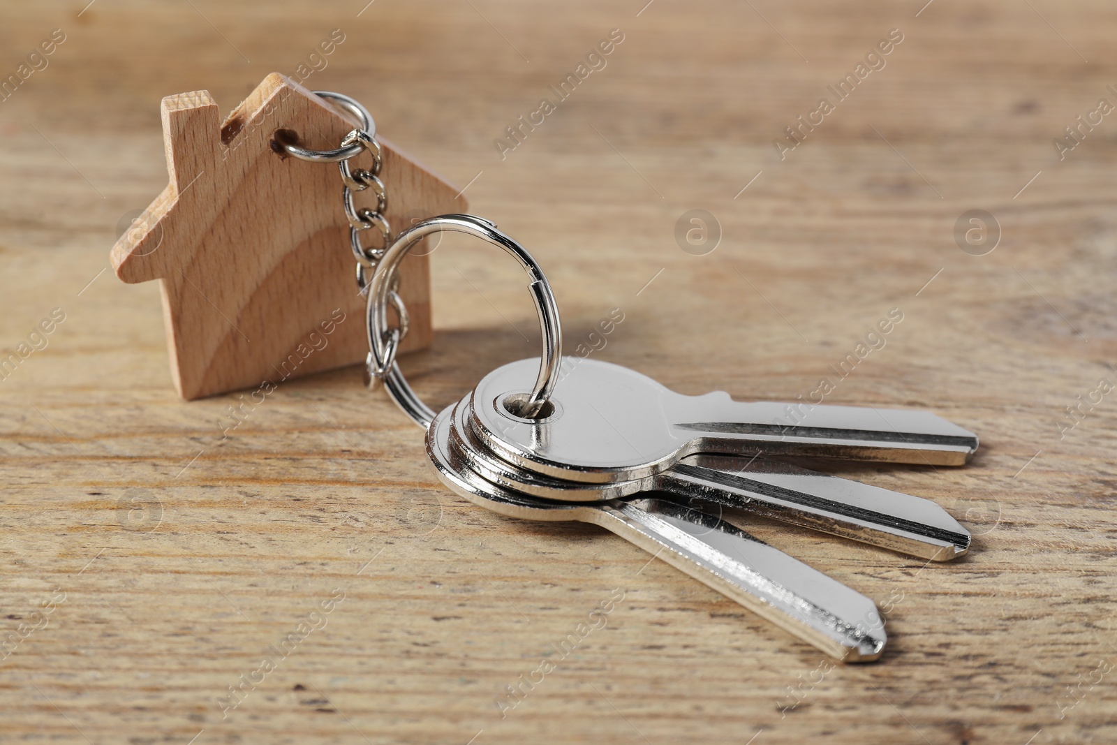 Photo of Keys with keychain in shape of house on wooden table, closeup