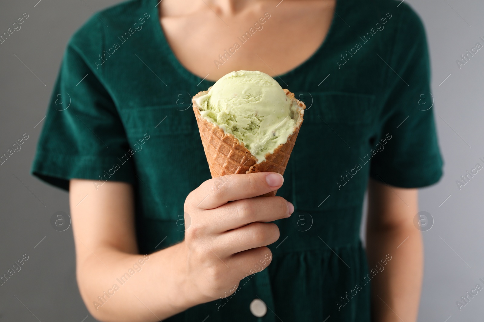 Photo of Woman holding green ice cream in wafer cone on grey background, closeup