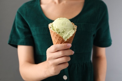 Woman holding green ice cream in wafer cone on grey background, closeup