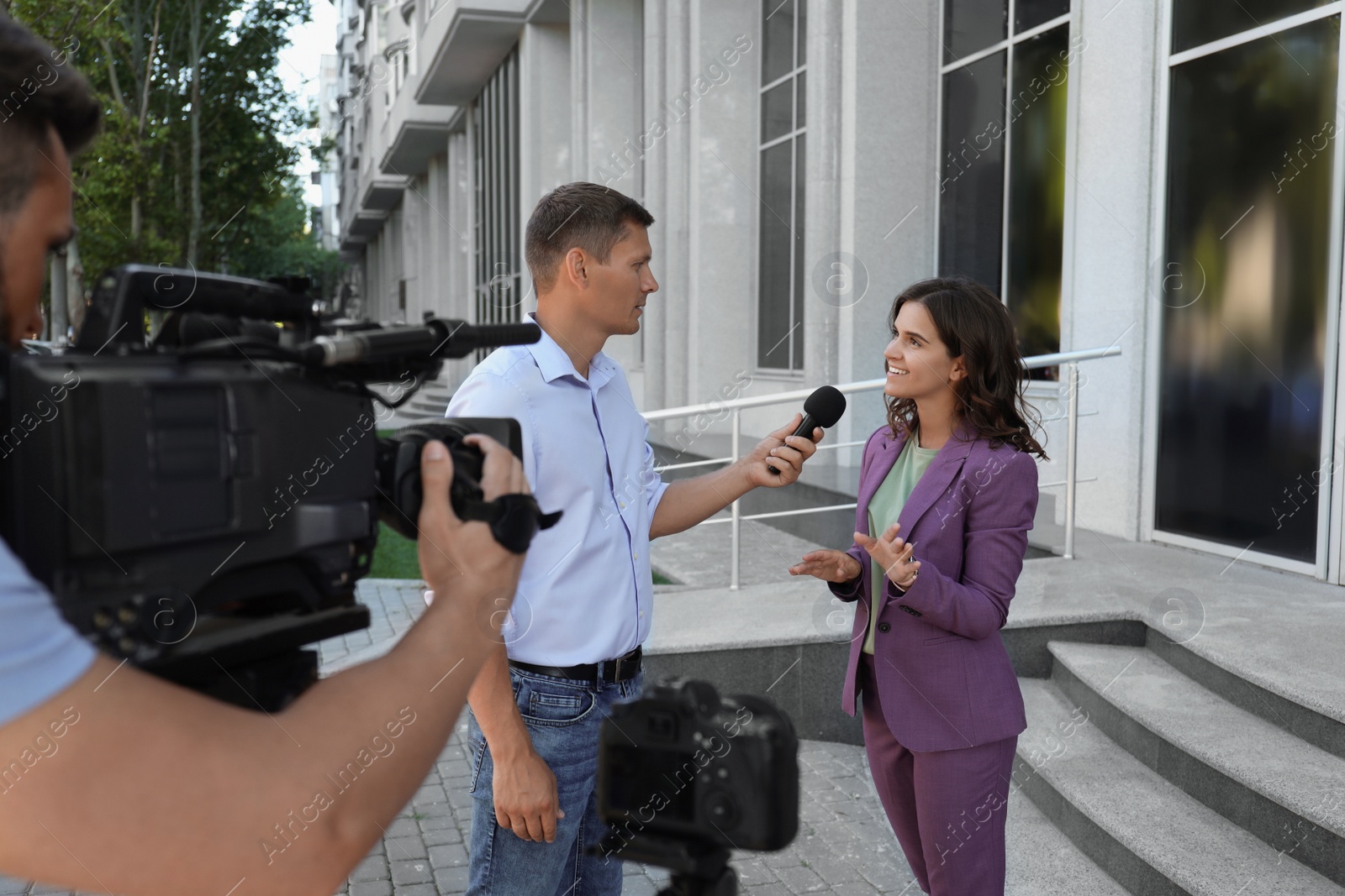 Photo of Professional journalist and operator with video camera taking interview outdoors