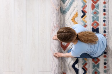 Photo of Woman unrolling carpet with beautiful pattern on floor in room, top view. Space for text