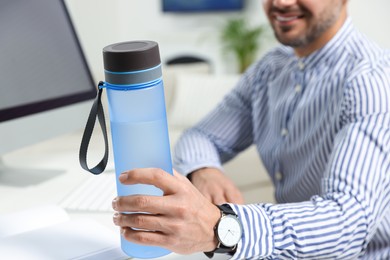 Photo of Man taking transparent plastic bottle of water while working on computer in office, closeup