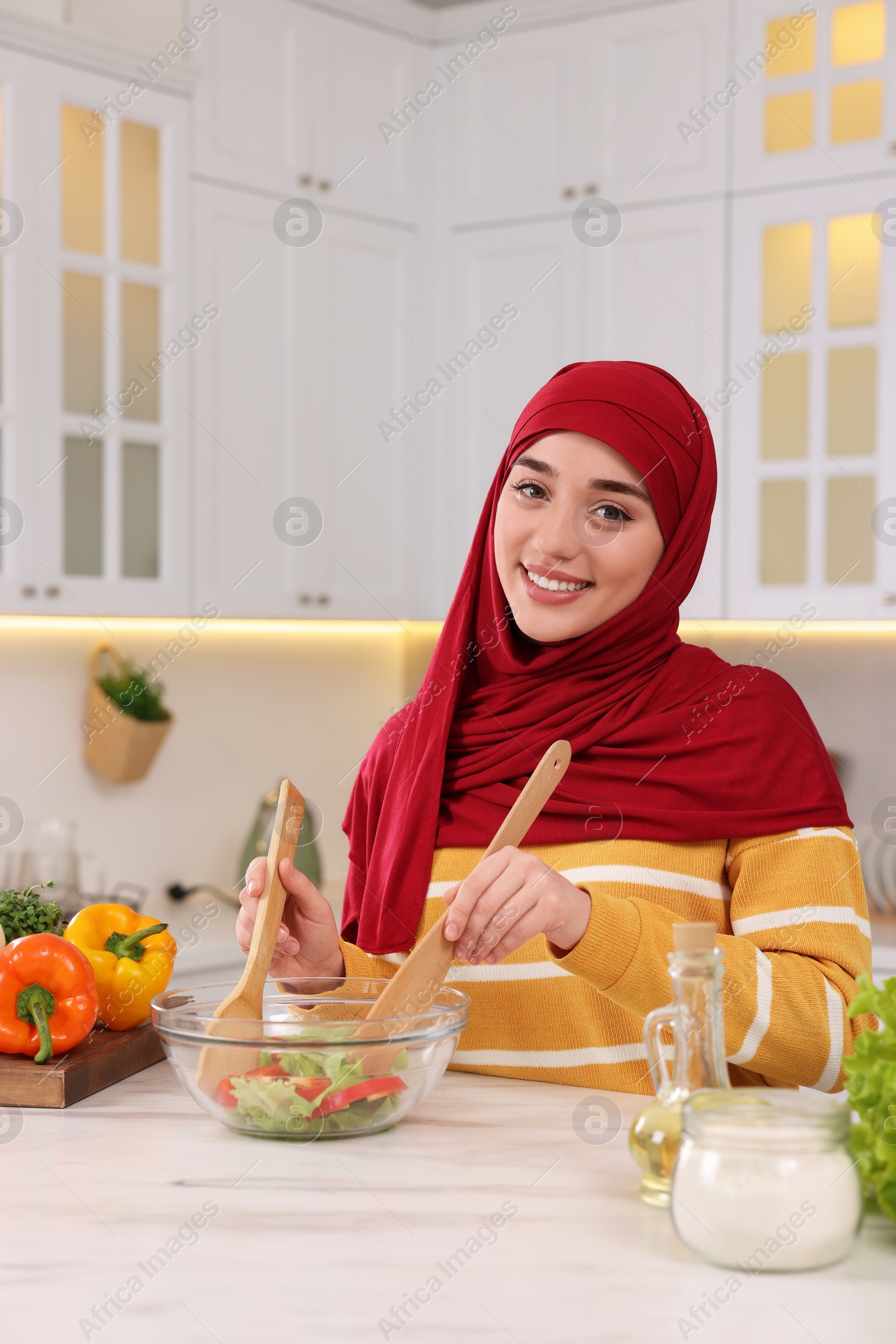 Photo of Muslim woman making delicious salad with vegetables at white table in kitchen