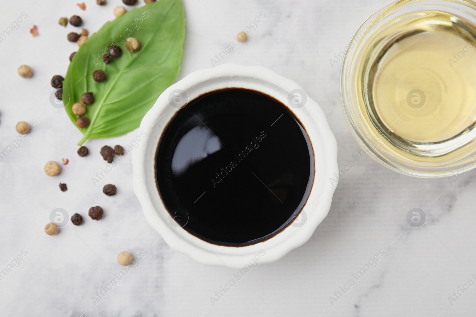 Photo of Bowl with balsamic vinegar and ingredients on white marble table, flat lay