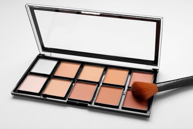 Photo of Colorful contouring palette with brush on light grey background, closeup. Professional cosmetic product