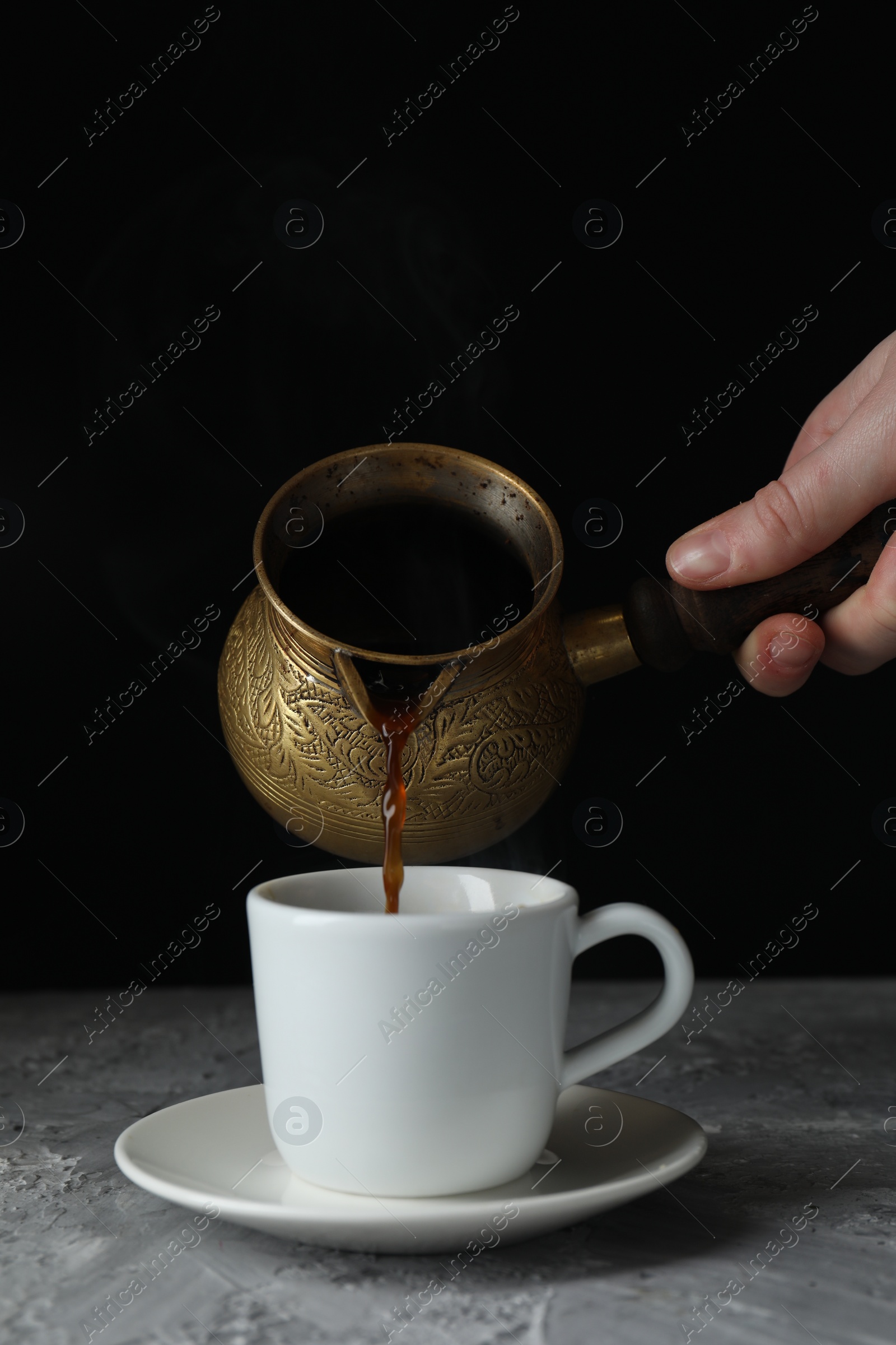 Photo of Turkish coffee. Woman pouring brewed beverage from cezve into cup at grey table, closeup