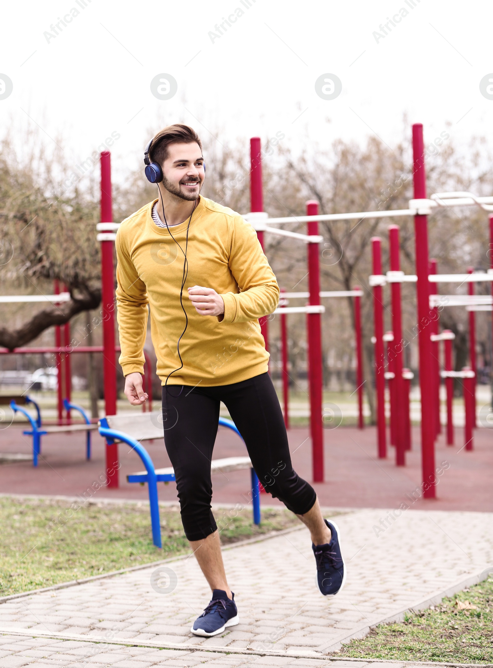 Photo of Young man with headphones listening to music and exercising on sports ground