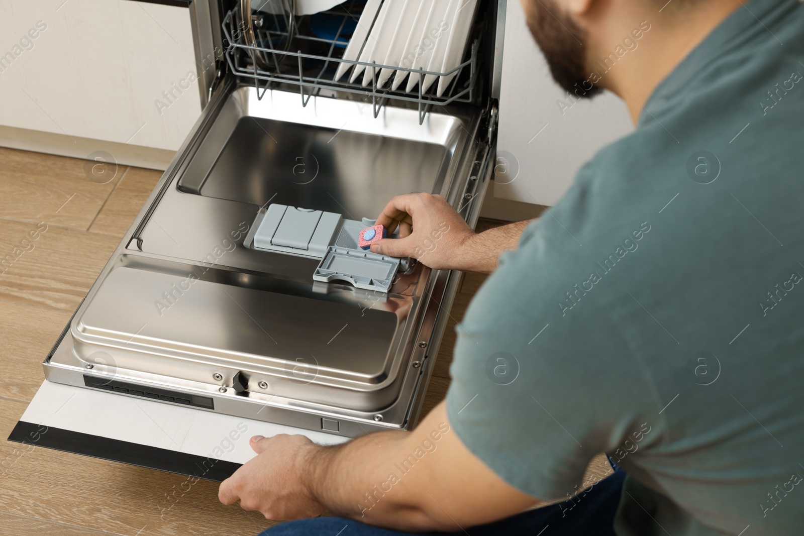 Photo of Man putting detergent tablet into open dishwasher, closeup