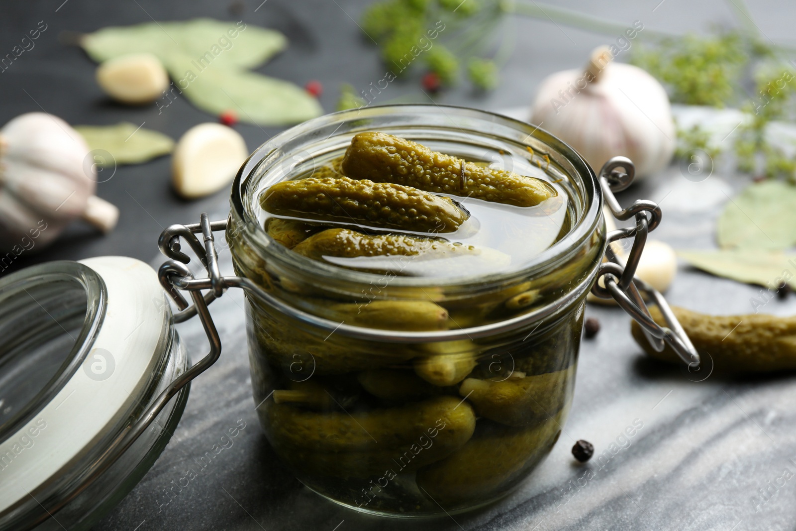 Photo of Glass jar of pickled cucumbers on grey board, closeup
