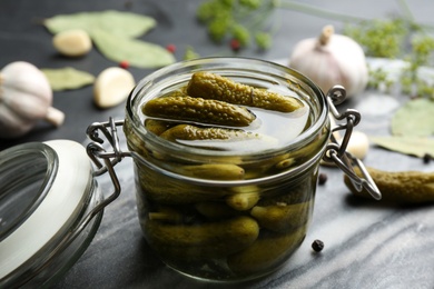 Glass jar of pickled cucumbers on grey board, closeup