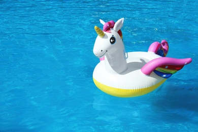 Photo of Funny inflatable unicorn ring floating in swimming pool on sunny day. Space for text