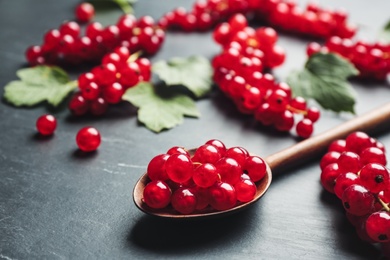 Wooden spoon with ripe red currants on black table, closeup