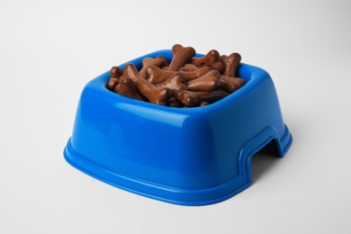 Photo of Blue bowl with bone shaped dog cookies on white background, closeup