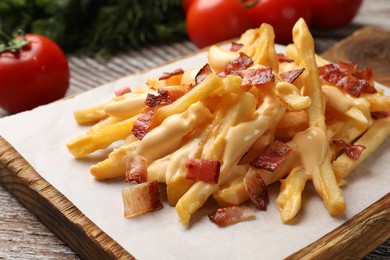 Photo of Delicious French fries with bacon and cheese sauce on wooden table, closeup