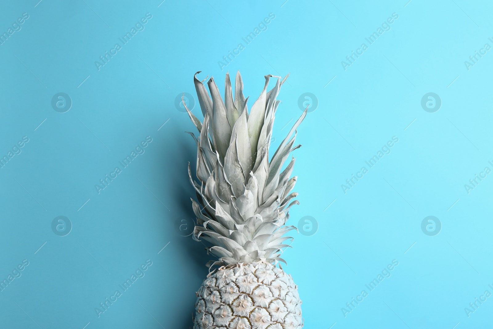 Photo of Painted white pineapple on light blue background, top view. Creative concept