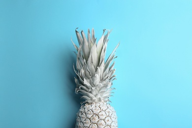 Painted white pineapple on light blue background, top view. Creative concept