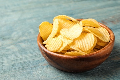 Delicious crispy potato chips in bowl on table, space for text