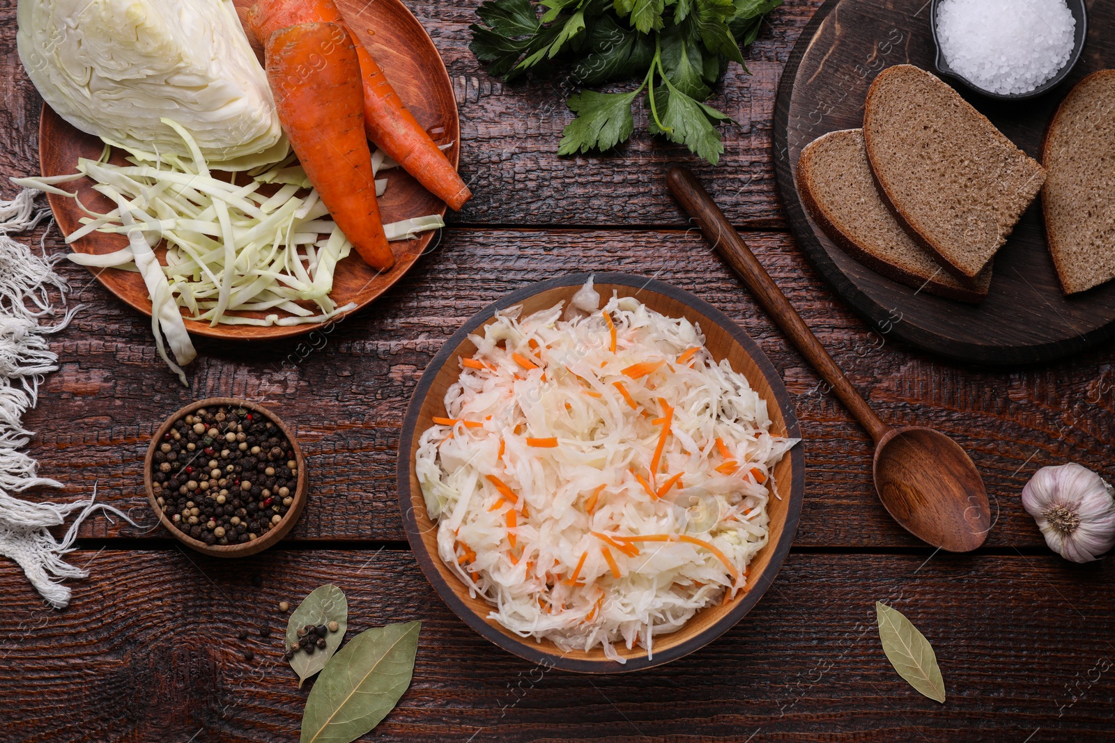 Photo of Bowl of tasty sauerkraut and ingredients on wooden table, flat lay